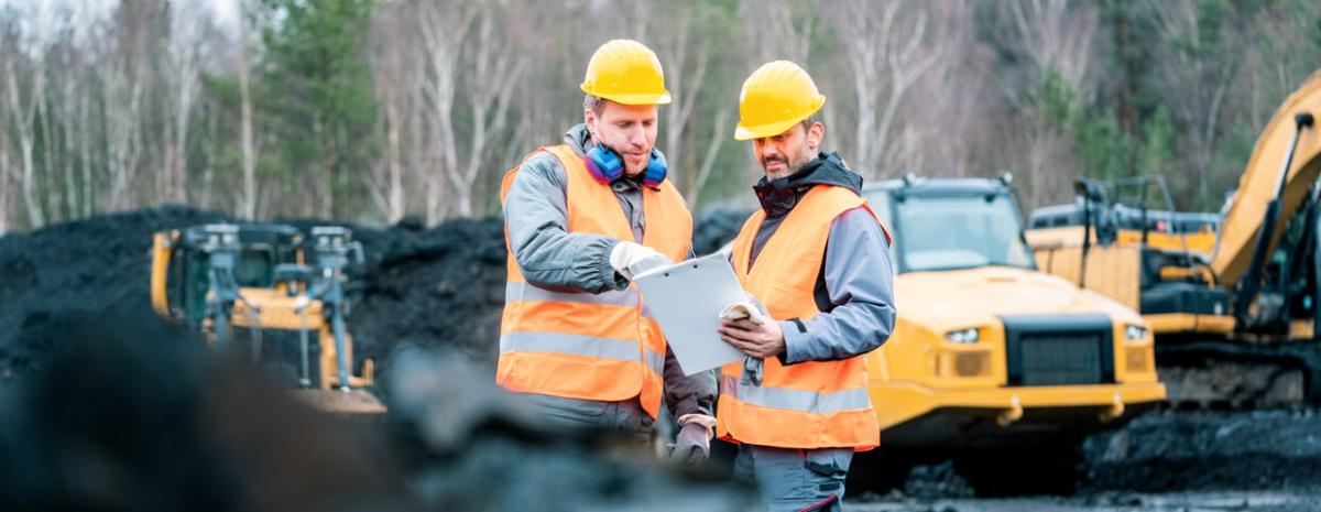 Workers in quarry, or surface mine, looking at a plan on clipboard