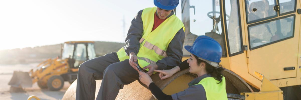 workers leaning on steamroller, looking at phone